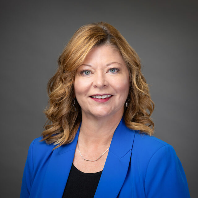 Portrait of Chris Ward with her hair down wearing a blue blazer.